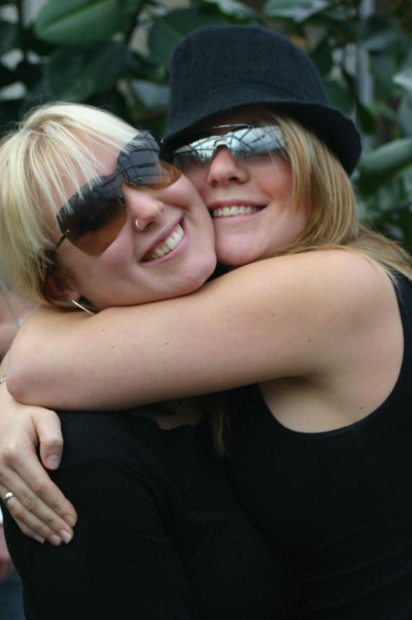 Två glada tjejer med solglasögon kramar varandra innerligt.