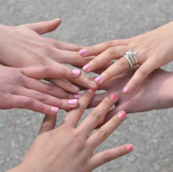 Fem händer där fingrarna har rosa nagellack och möts tillsammans.