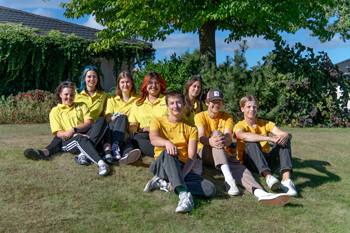 Åtta ungdomar i gula tröjor sitter tillsammans på gräsmattan