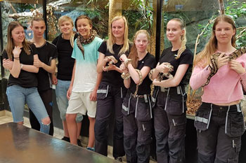 Åtta ungdomar står framför ett terrarium och flera av dem håller i ormar