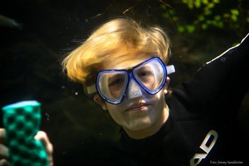 Pojke  med cyklop och våtdräkt i ett stort  akvarium