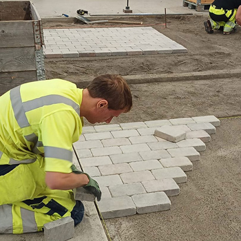 En kille sitter p&aring; huk vid en plattl&auml;ggning