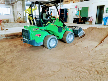 Elev kör en liten grön lastmaskin i en markanläggningshall med sand