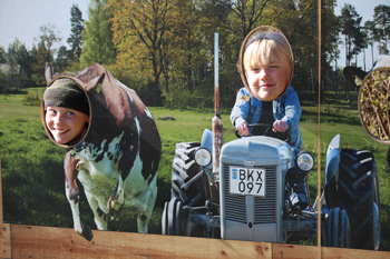 Två barn  i en tavelbild med traktor och ko