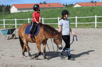 Ett barn leder en ponny med ett ridande barn