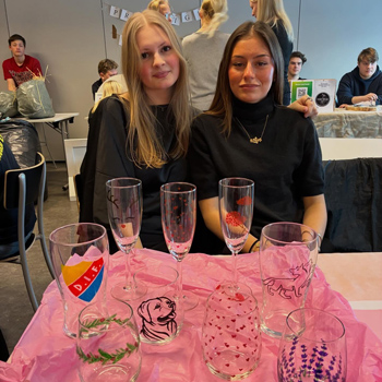 Tv&aring; inga flickor sitter vid ett bord med dricksglas p&aring;